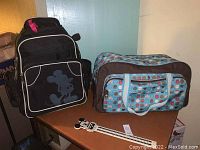 Photo of black Mickey Mouse rolling backpack, patterned duffel bag, and Mickey Mouse ruler on a table.