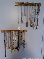 Photo showing two wooden racks mounted on wall holding about 20 necklaces and pendants made with beads, leather cords, carved stones.