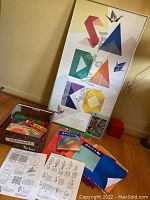 Framed Sadako poster, origami paper packs, origami instruction sheets, book and a small string of cranes displayed on floor.