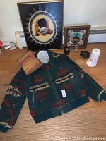 Vintage Pendleton wool coat laid flat with art prints, pillow, candle lamp, and magnets arranged behind it on the floor.