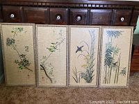 Four signed Japanese art prints arranged side by side showing paintings of floral and bamboo subjects with carved wooden frames.