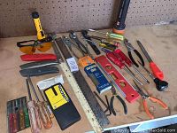 Assorted hand tools laid on a workbench including multiple screwdrivers, pliers, levels, handsaw, ruler and safety glasses