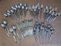 Full layout of all 58 pieces in the flatware set showing spoons, forks, knives, and serving utensils arranged separately on a flat surface