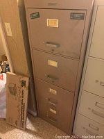 Front view of the beige metal file cabinet with four drawers, showing handles and label holders.