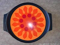 Top view of vintage Rubbermaid tray showing orange and red sunburst design on black base with handles.