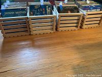 Four wood crates filled with vinyl records (records not included in lot). Crates rest on a wooden floor, showing front and side view details of the slatted design and natural wood tone.