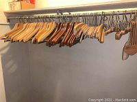 Wide view of assorted wooden hangers including natural and dark wood on a metal clothing rod