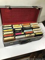 Open vintage black carrying case displaying multiple colorful 8 track tapes arranged in rows inside a red fabric interior