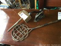 Photo of the large wooden mallet, cast metal stamp press lever, and wicker rug beater on a wooden surface.