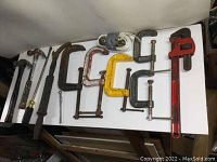 Full view of all tools laid out on table including clamps, wrenches, hammers, screwdriver, nail puller and ratchet strap