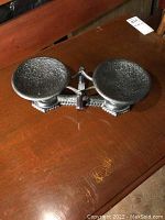 Front angled view of the antique cast iron balance scale showing the two rounded weighing pans and central balance beam with textured surface.