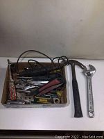 Photo showing Dremel Moto Tool, assorted hand tools and sockets in a cardboard box, claw hammer, and Fuller adjustable wrench on table.