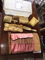 Vintage French ivory dresser set including trinket box, manicure set in pink lined case, shoe horn, brush, and picture frame laid out on table