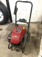 Front view of the pressure washer showing red engine cover, frame and wheels