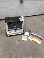 Overview shot of Kero-Sun kerosene heater with five new wick packages and instruction booklet displayed on concrete floor.