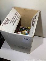 White cardboard box open at top filled with hundreds of vintage match packages visible inside, various colors and designs.