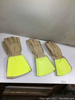 Three pairs of tan leather work gloves with yellow cuffs displayed side by side on a white surface.