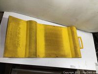Yellow Park Smart parking mat, top view showing embossed text and shape with raised humps and handle