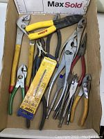 Photo of various pliers, wire strippers, cutters and drill bits in a box showing assortment and condition.