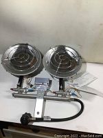 Front view of dual head propane heater showing two burner heads with protective grills, metal frame, attached hose and valve.