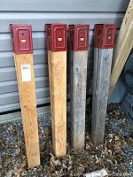 Two pairs of wooden saw horse legs standing upright, showing natural wood and weathered wood color with red metal brackets on top.