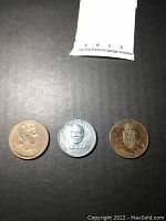 Three older large size coins laid out on a dark surface; front sides visible showing different designs.