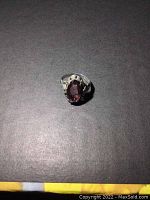 Front angle view of sterling silver ring with oval amethyst colored stone on black background.
