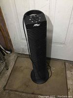 Front angle view of black tower fan showing front grill and base on floor.
