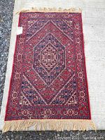 Full view of vintage oriental-style rug showing pattern and fringe, laid on pavement and gravel
