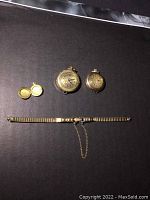 Overview of two pendant watches, small locket pendant, and Speidel wrist watch band on dark background.