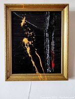 Front view of framed abstract painting: black textured background with gold and red splashes.