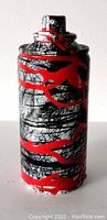 Front view of spray can sculpture showing black and white marbled texture with red paint drips and lines.