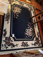 Full view of floral pattern area rug with dark center and cream border, showing floral clusters and fringe.