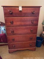 Front view of the five drawer wooden dresser showing the drawers, round knobs, and worn finish with scratches.