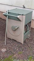 Green Ames ReelEasy reel hose storage box outdoors, showing side and front with attached garden hose extending.