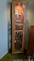 Full view of wooden display cabinet with glass door containing porcelain, figurines, and pewter pieces.