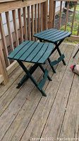 Two green plastic collapsible side tables on wooden deck.