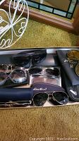 Top view of multiple pairs of men's sunglasses with cases, showing different frame styles and brand cases including Eddie Bauer.