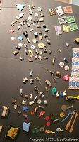Photo showing an assortment of small collectible Cracker Jack prize figurines, charms, miniature toys, whistles, coin-like items, a Coca-Cola pin, and other trinkets arranged on a dark surface.