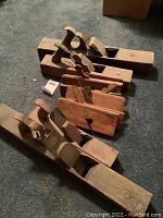 Photo showing all 9 wooden hand planes aligned on floor, with visible various sizes and wooden handles.