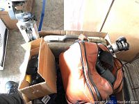 Photo showing tripods, brown leather camera bag, and packed boxes