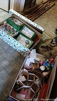 Box containing assorted Christmas ornaments and decor including multiple green boxed ornaments and other mixed decorations