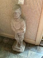 Photo showing full view of the cement Civil War soldier statue standing against wall on tiled floor.