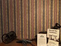 Showing two miniature Civil War cannons, one with a caisson, placed on a wooden surface against a patriotic striped wallpaper.