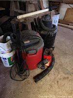 Two wet/dry shop vacuums including a red Craftsman model and a black vacuum with hose and accessories on the floor, needing cleaning and unknown working condition.