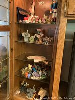 Wide view of wooden cabinet with multiple shelves filled with various elephant figurines and other miniatures mostly ceramic, glass, and stone materials.