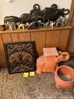 Wide view of terra cotta elephant stand and round planter alongside various elephant figurines on floor and against wall.