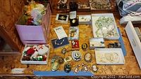 Full overview of assorted vintage jewelry including cameo brooches, rings, necklaces, and small boxes with pins and other pieces on a wooden surface.
