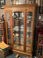 Front view of oak display cabinet showing double glass doors, dentil molding, and base