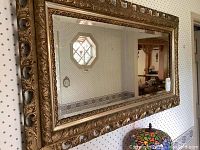Full view of large rectangular vintage mirror with gold gilt carved wood frame hanging on wall.